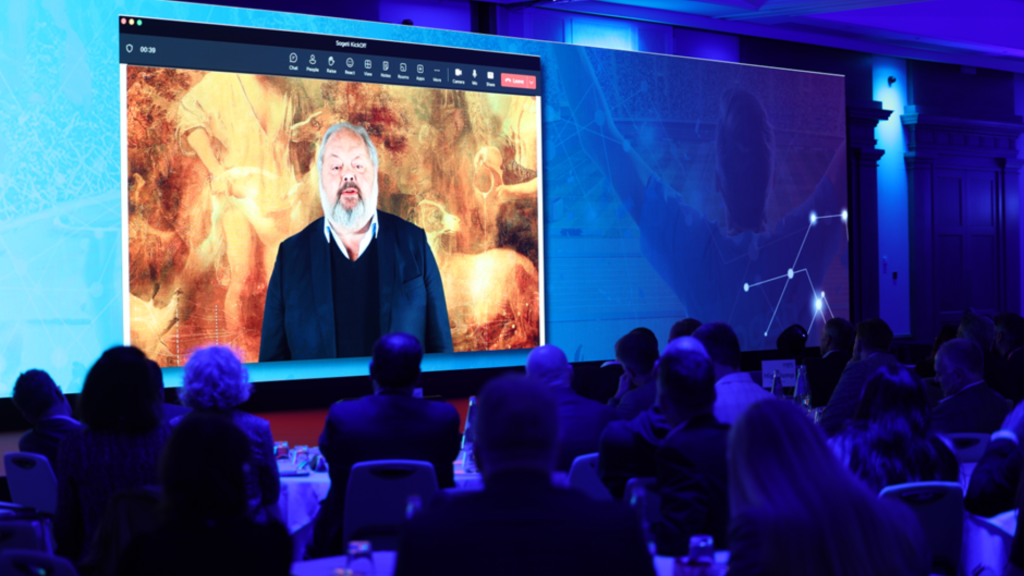 A group of people sitting at tables in front of a large screen.
